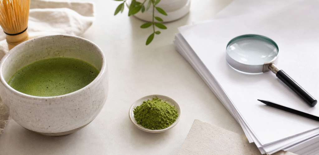 Prepared matcha and powder beside blank research papers and a magnifying glass